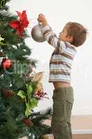 Hes decorating the tree on his own this year. Shot of a young boy decorating a christmas tree by himself.