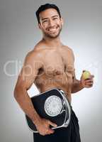 Im doing everything I can to maintain a healthy weight. Shot of an athletic young man holding an apple and a weighing scale.