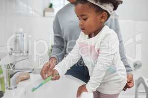 Learning all about good hygiene from a young age. Shot of a mother helping her little daughter rinse her toothbrush at a tap in the bathroom at home.