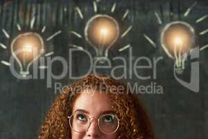 Shes full of bright ideas. Shot of an attractive young businesswoman standing in front of chalk drawings of lightbulbs on a chalkboard.