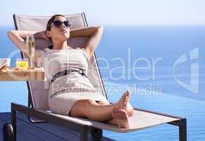 Relaxing while on holiday. A posh young woman reclining on a deck chair with her hands behind her head.