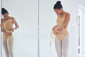 Restrictions in the industry. Shot of a beautiful young ballet dancer measuring her waist during a rehearsal.