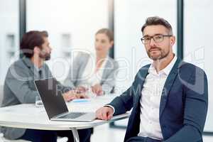 Were all about inspiring innovation. Portrait of a businessman sitting in a boardroom meeting with colleagues in the background.