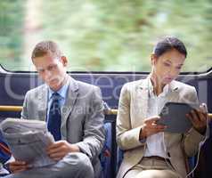 Optimizing their travel time wisely. Two business people reading catching up on the news on their commute to work.