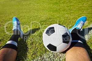 Eat, sleep, play soccer. POV shot of a soccer player sitting with a soccer ball on a playing field.