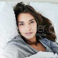 Nothing can spoil my day today. Portrait of an attractive young woman taking a self portrait with her cellphone while lying in bed at home.