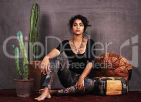 Ethnically at ease. Studio portrait of a beautiful young woman sitting amongst cacti and cushions.