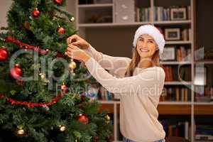 Getting everything ready before everyone gets here. Shot of a beautiful young woman decorating her Christmas tree at home.