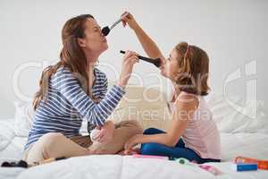 Excuse me while I powder your nose. Shot of a mother and her daughter playing with makeup on the bed.