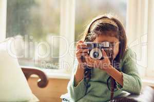 Who knows where her hobby might lead her. Shot of a little girl taking pictures with a vintage camera at home.