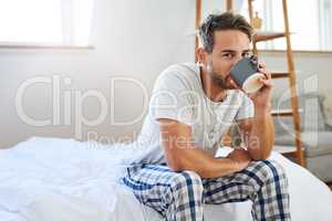 The day doesnt start until that first sip. Shot of a handsome young man drinking coffee in bed at home.