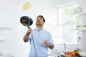 You gotta have fun with your food. Shot of a young man making pancakes at home.