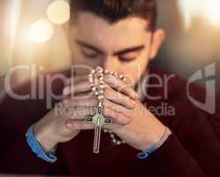 I cant do it on my own. Shot of a young man praying on his own while holding a rosary.