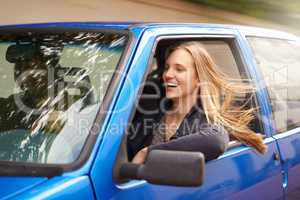 On the road. A young woman feeling the wind in her hair through an open car window.