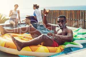 The cool guy wishes everyone a happy holiday. Portrait of handsome young man raising up his glass for a toast while relaxing in a pool outdoors with friends.