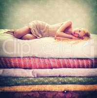 Is there a pea under these. Portrait of an attractive woman lying on a bed of stacked blankets.