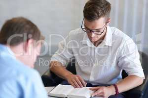 Belief is an important factor in any aspect of life. Shot of two young businessmen reading their bibles at work.