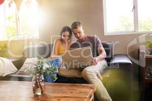Home is where the hotspot is. Shot of a happy young couple using a laptop together on the sofa at home.