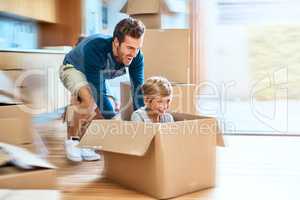 Off we go in the spaceship. Shot of a cheerful young man pushing his son around in a box imagining its a car inside at home during the day.