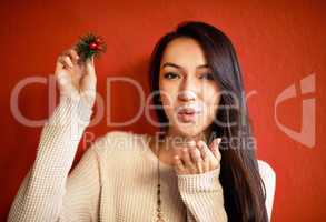 This kiss is for you.... An attractive young woman holding up a holly branch while standing against a red wall.