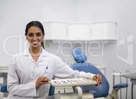 Oral health is an essential part of a healthy life. Portrait of a young female dentist sitting alongside a tray of surgical instruments in her office.