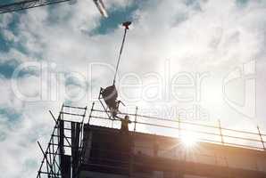 The more powerful the equipment, the more powerful the finish. Shot of a man lifting heavy machinery with a crane at a building site.