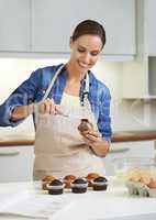 Putting its the icing on the cupcake. A happy young woman about to apply frosting to her freshly-baked batch of cupcakes.