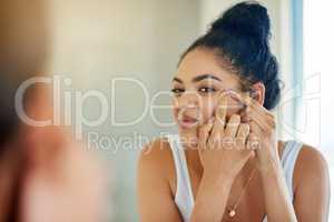 One pimple can change your entire day. Shot of a young woman squeezing a pimple in front of the bathroom mirror.