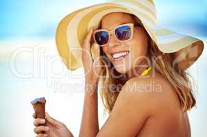 Ice cream is the perfect summer companion. Portrait of a beautiful young woman eating an ice cream at the beach.
