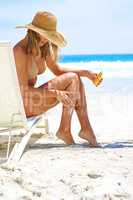 Taking care of her skin. Full length shot of a young woman applying suntan lotion while relaxing at the beach.