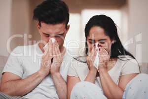 In sickness and health. Cropped shot of a young couple blowing their noses while sitting on the living room sofa.