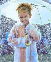 This is so exciting. Shot of a little girl playfully standing in the rain holding her umbrella.