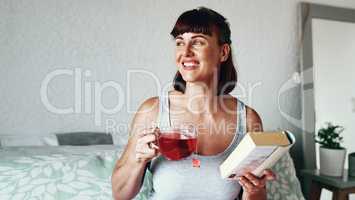 Good books capture the imagination. Shot of an attractive young woman drinking tea and reading a book in her bedroom at home.