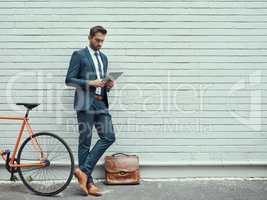Places to go, successes to be made. Shot of a handsome young businessman using a digital tablet while standing alongside his bike outdoors.
