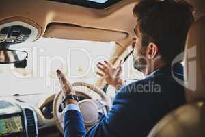 I cant believe how many cars are on the road. Shot of a stressed young businessman holding up his hands in frustration while driving in his car and sitting in traffic.