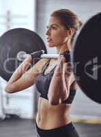 Challenging her body. Shot of a young woman working out with weights at the gym.