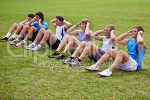 Abdominal muscles of steel. Shot of a row of young sportsmen doing sit-ups.