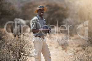 Never a dull moment on the job. Portrait of a confident game ranger looking at a group of rhinos in the veld.