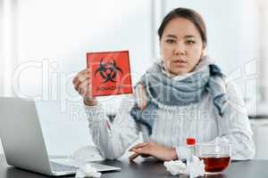 We should all be safety conscious during this crisis. Shot of a young businesswoman holding a biohazard sign at her desk in a modern office.