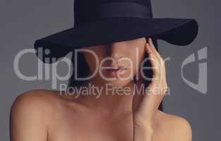 Shes a mystery. Studio shot of a beautiful woman wearing a hat against a gray background.