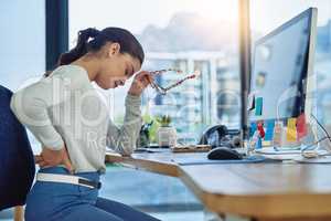 Trying to get through the aches of a hard day. Shot of a young businesswoman suffering from back pain while working in an office.