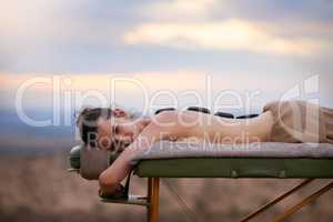 Hot stones will mend these tired bones. Portrait of a young woman receiving a hot stone treatment on a massage table outside.