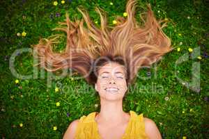 When youre happy everyday is a good hair day. High angle shot of a carefree young woman relaxing in a field of grass and flowers.