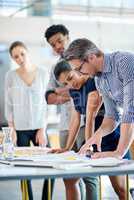 Leading the way with creative collaborations. Male and female managers planning at a table with younger staff members looking on.