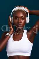 Beast mode activated. Cropped portrait of an attractive young sportswoman standing alone and posing with headphones on against a dark studio background.