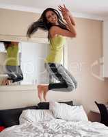 Jumpstart your mornings with an energy boost. Portrait of an energetic young woman jumping on the bed at home.