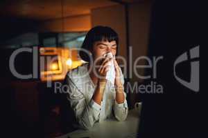 Risking her health for the sake of the deadline. Shot of a young businesswoman blowing her nose during a late night at work.