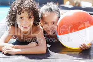 Enjoying the sun and a swim. Portrait of two children lying by a swimming pool on a sunny day.