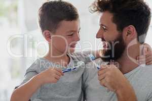 Got to keep the tooth decay at bay. Shot of a father and his little son brushing their teeth together in the bathroom at home.