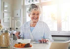 Happy at home. Cropped shot of a senior woman using a digital tablet while having breakfast at home.